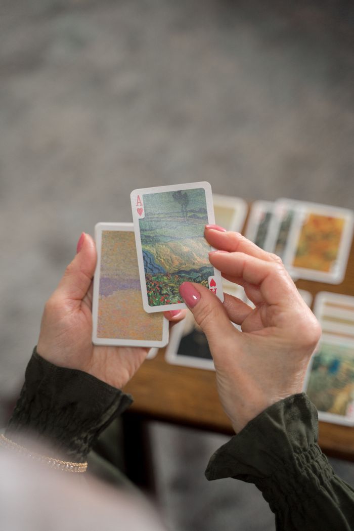 Hands of an unrecognizable woman holding artistic playing cards indoors.