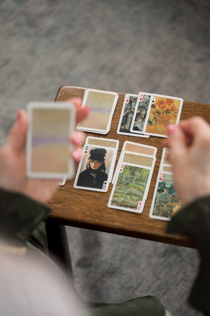 Close-up of hands engaged in solitaire with artistic playing cards on a wooden table.