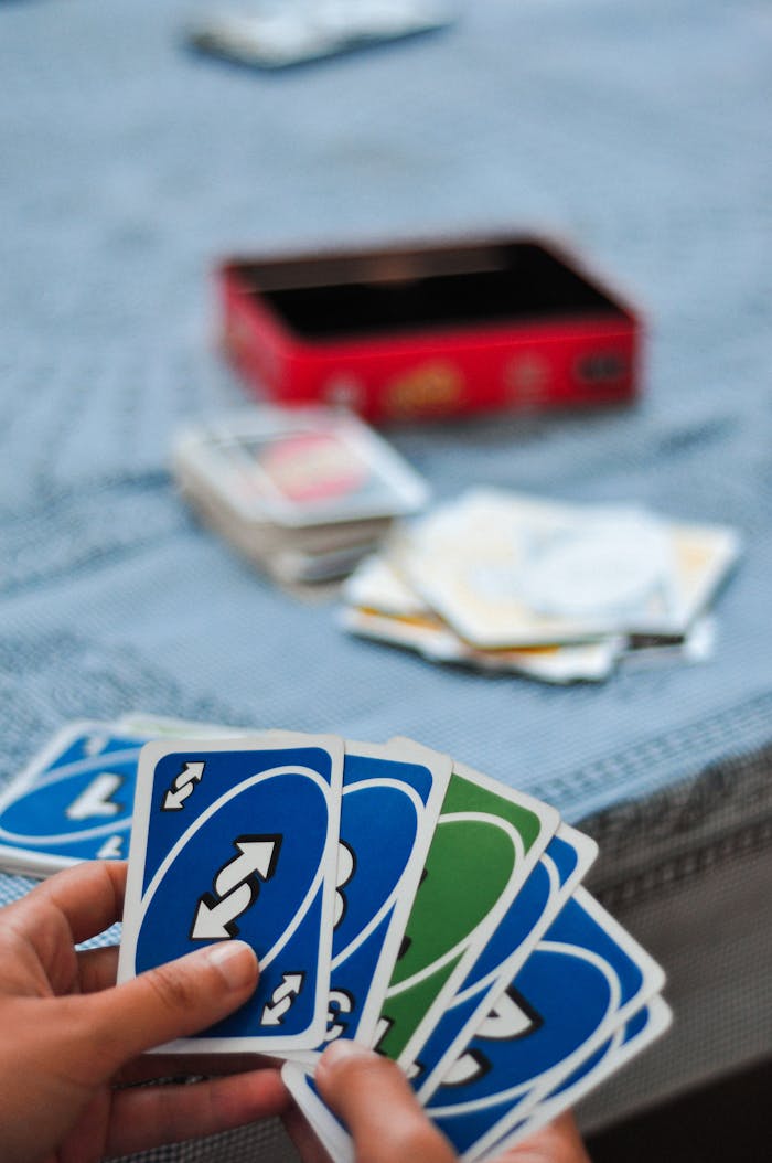 Hands holding and playing Uno cards with a blurred background on a table.