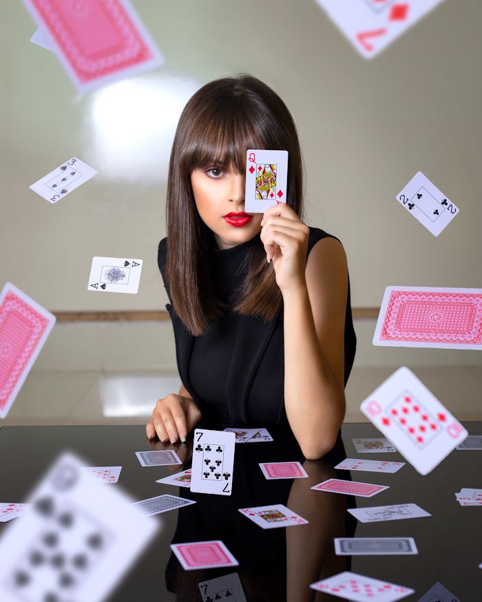 Crop female with card at face sitting at table with various playing cards floating in air while looking at camera